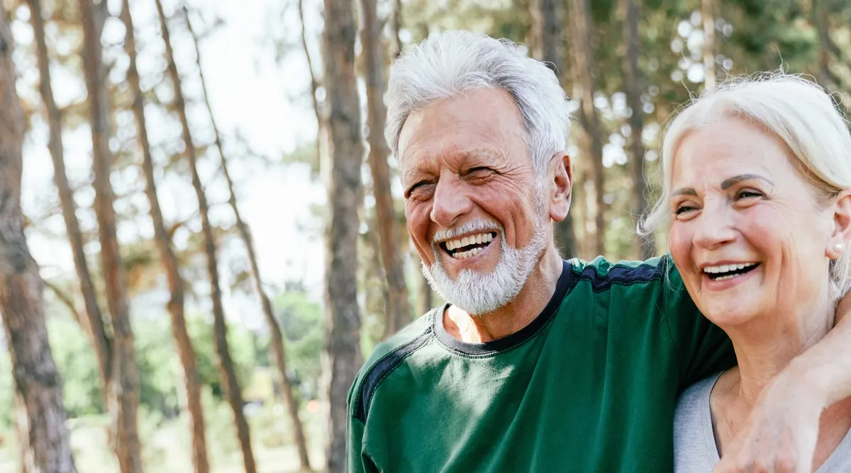 Smiling older couple walking together through a pine forest